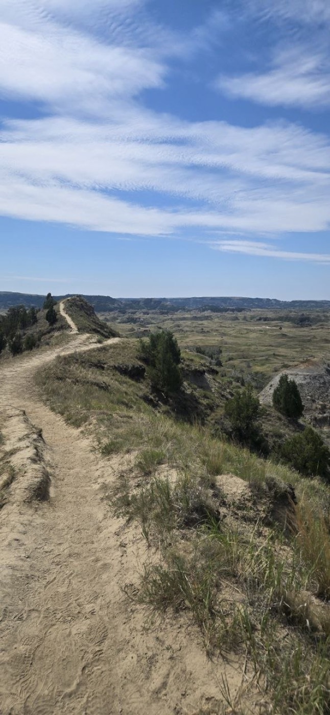 A sandy trail following a narrow ridge with badlands scenery falling away on both sides