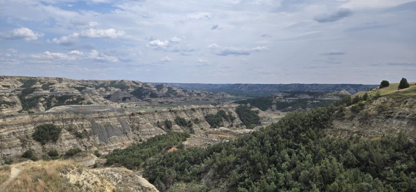 A wide badlands basin along the Caprock Coulee loop, with layered buttes and scattered junipers