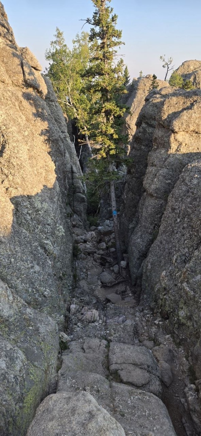 A narrow rocky chute between granite boulders, part of the scramble section near the summit