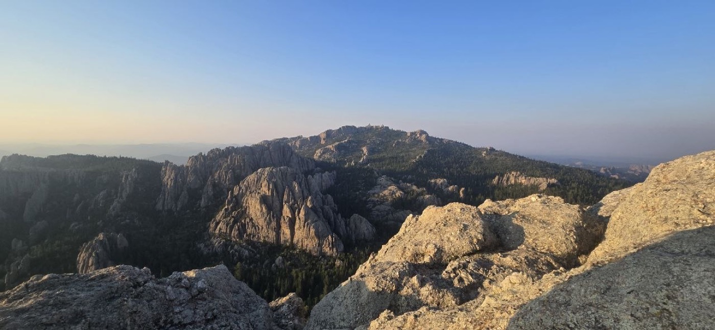 A wide view across a forested ridge toward distant rock formations, seen from near Little Devils Tower