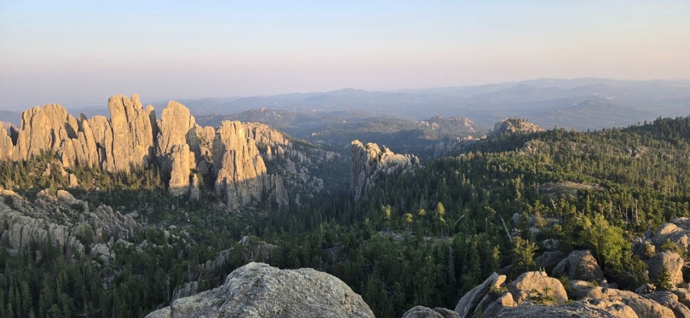 Golden evening light across the Black Hills, with distant granite spires visible on the horizon