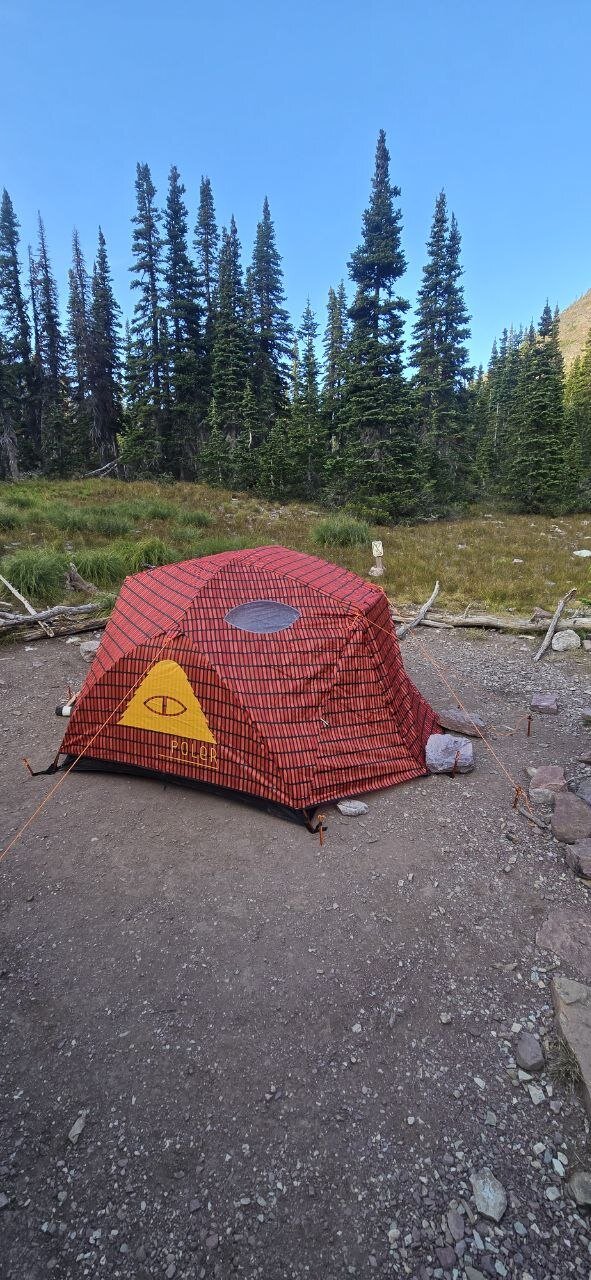 A red and black Poler tent pitched in a meadow near Cobalt Lake, Glacier National Park.