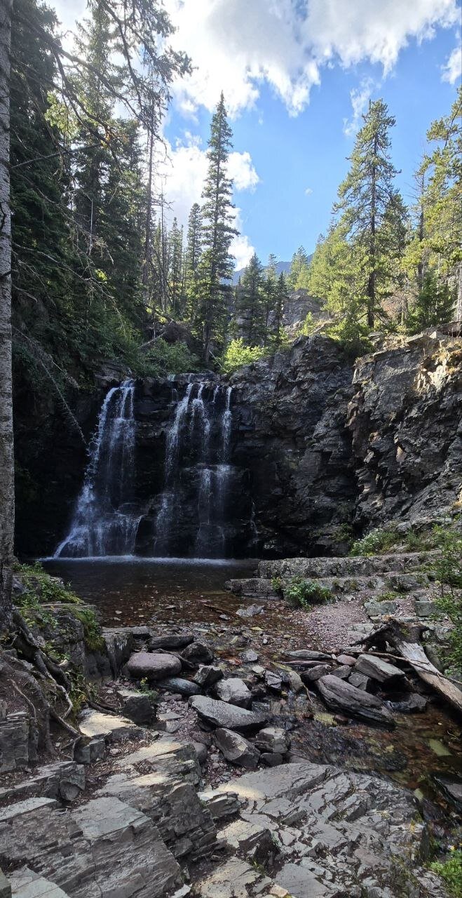 Rockwell Falls cascading over dark rock along the Cobalt Lake Trail.