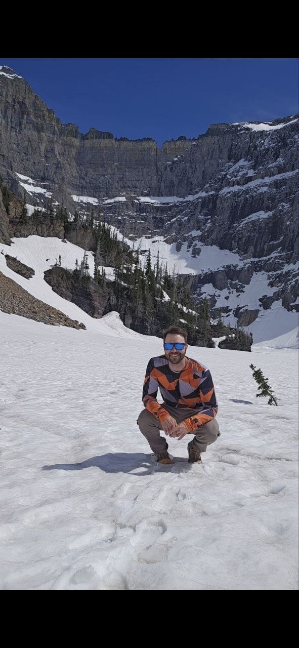 Standing in a high alpine snow bowl below towering cliffs in Glacier National Park.
