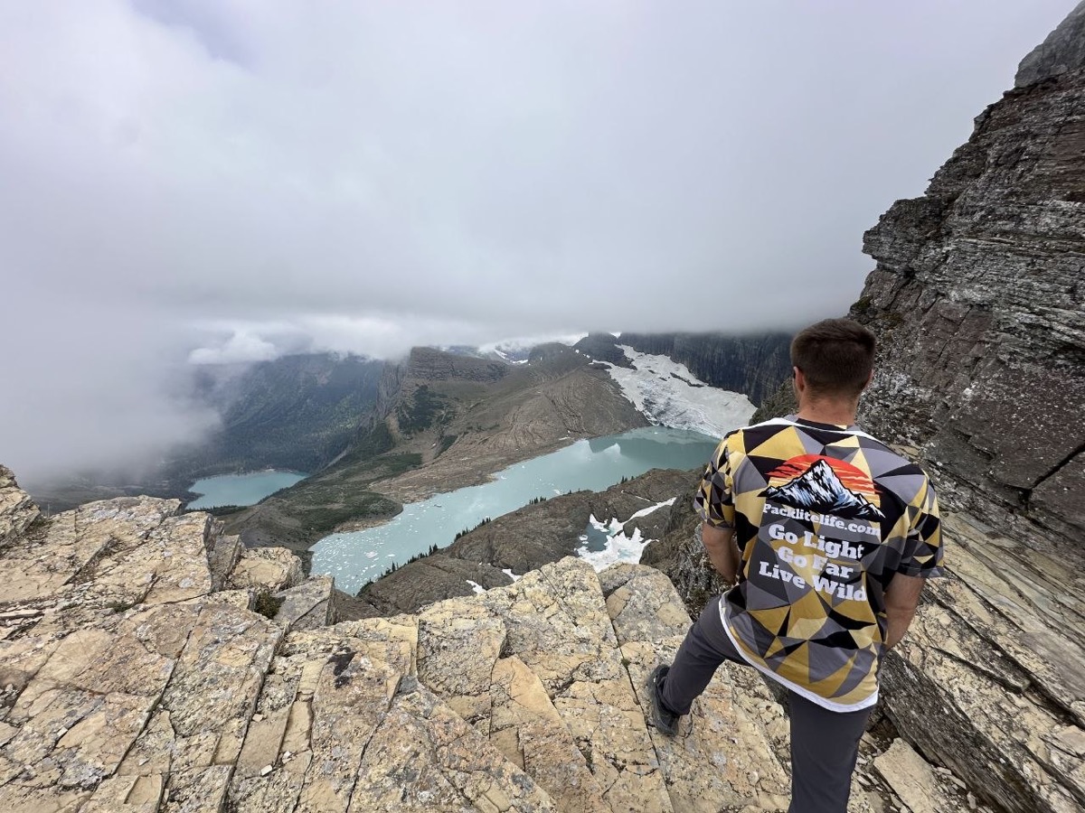 Looking out over Grinnell Glacier and the lake below, wearing the PackLite Life jersey with its mountain graphic and Go Light Go Far Live Wild back print