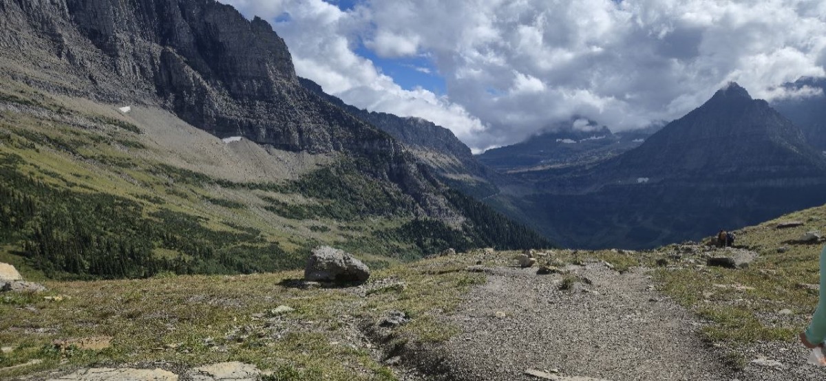Rocky trail with a wide mountain valley view along the Highline Trail near Logan Pass