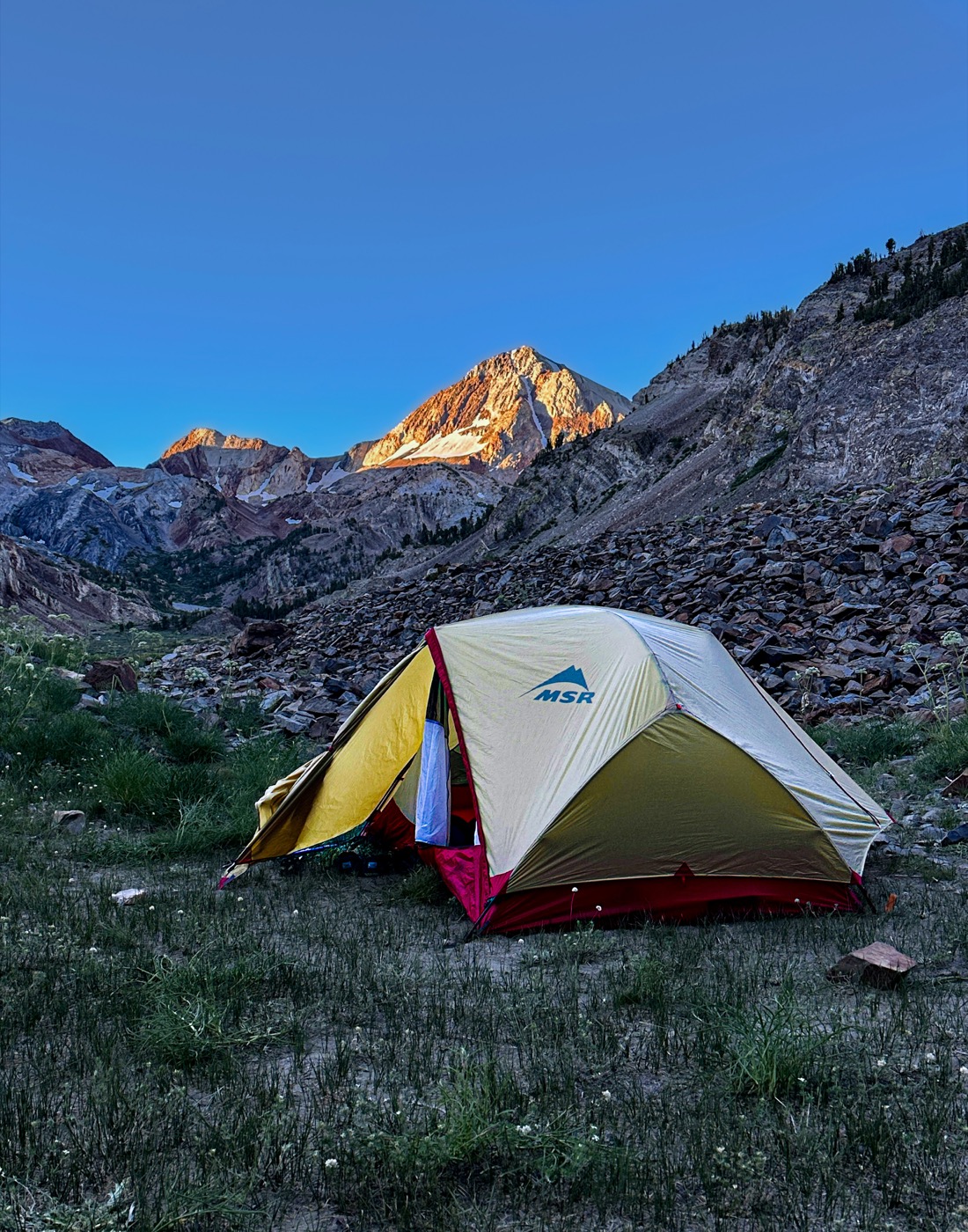 An MSR tent pitched in a rocky alpine basin at sunset, with a glowing peak in the background